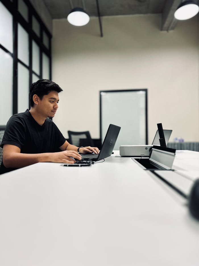 Young man focused on his laptop in a sleek, modern office setting, perfect for business themes.