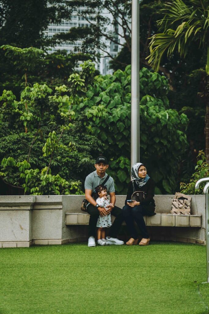 A family sitting on a bench in a lush green park in Kuala Lumpur, Malaysia.
