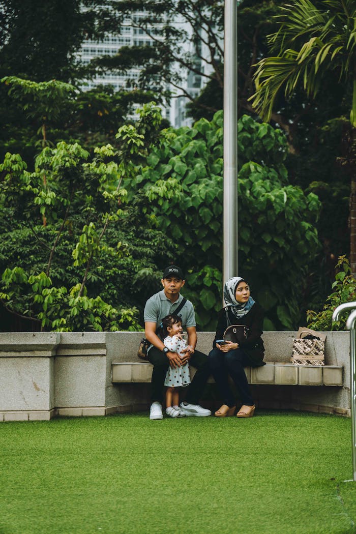 A family sitting on a bench in a lush green park in Kuala Lumpur, Malaysia.